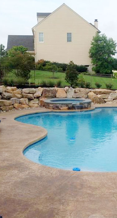 A pool with a stone wall and a hot tub.