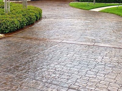 A brick driveway with bushes and trees in the background.