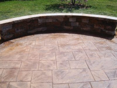 A brick patio with a stone wall and a tree.